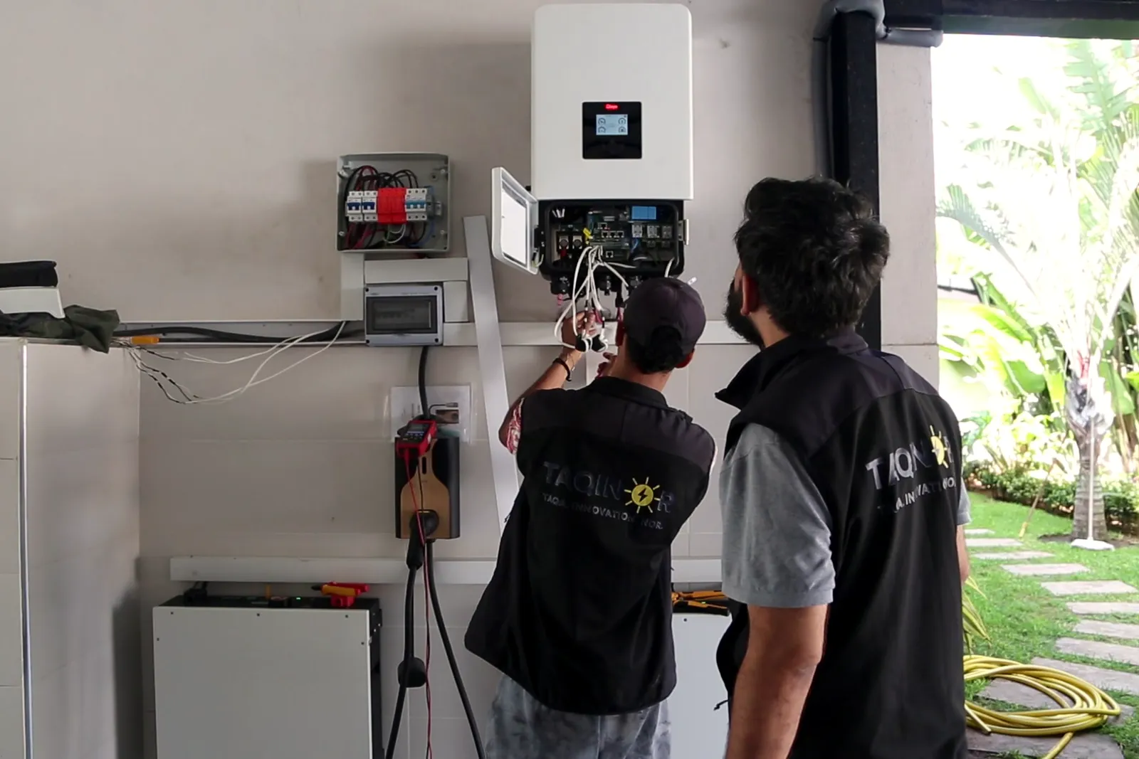 Deux installateurs Taqinor devant l’onduleur et le tableau électrique, chantier de Bouskoura
