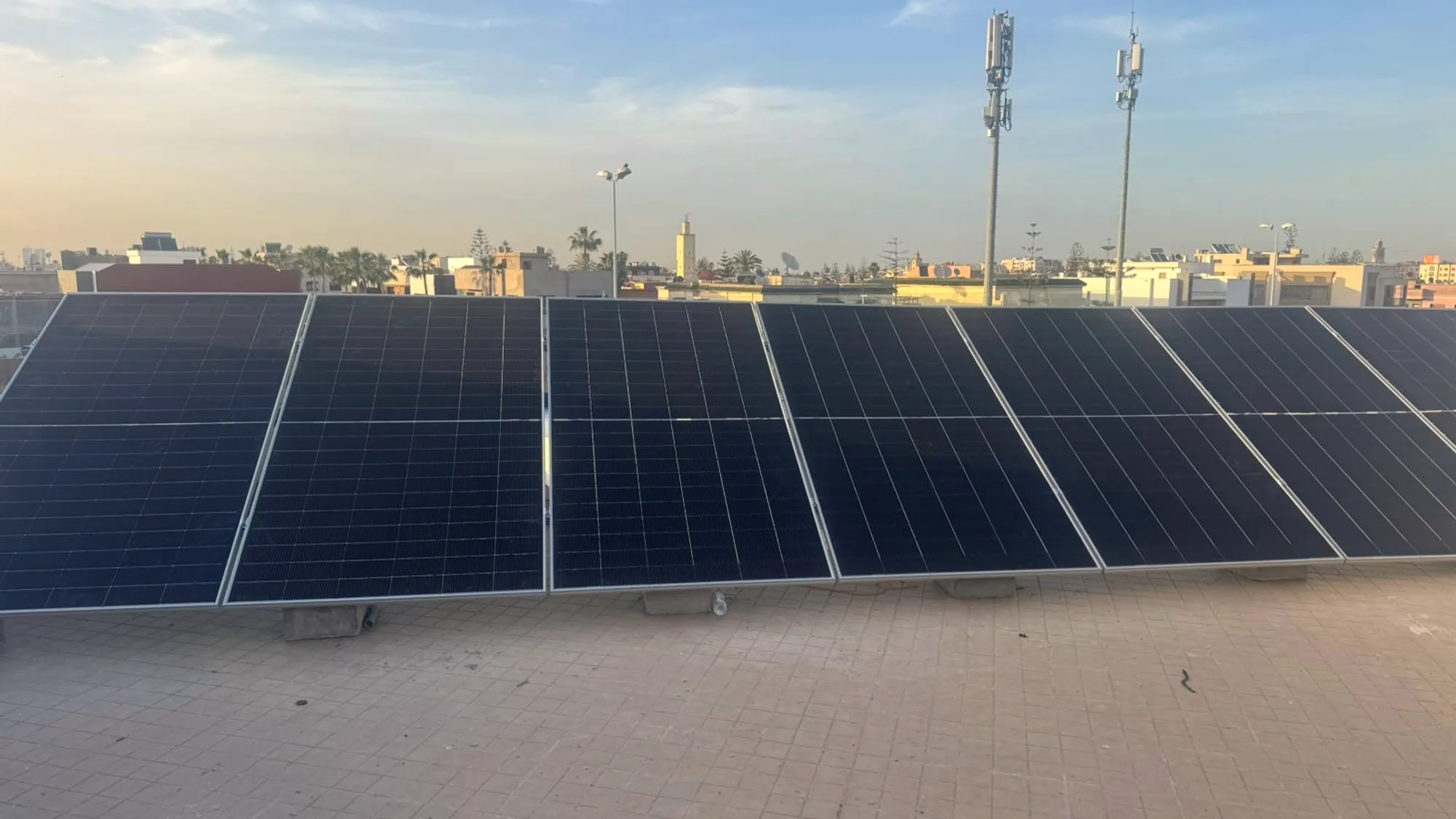 Rangée de panneaux solaires devant la skyline de Casablanca et un minaret, lumière dorée