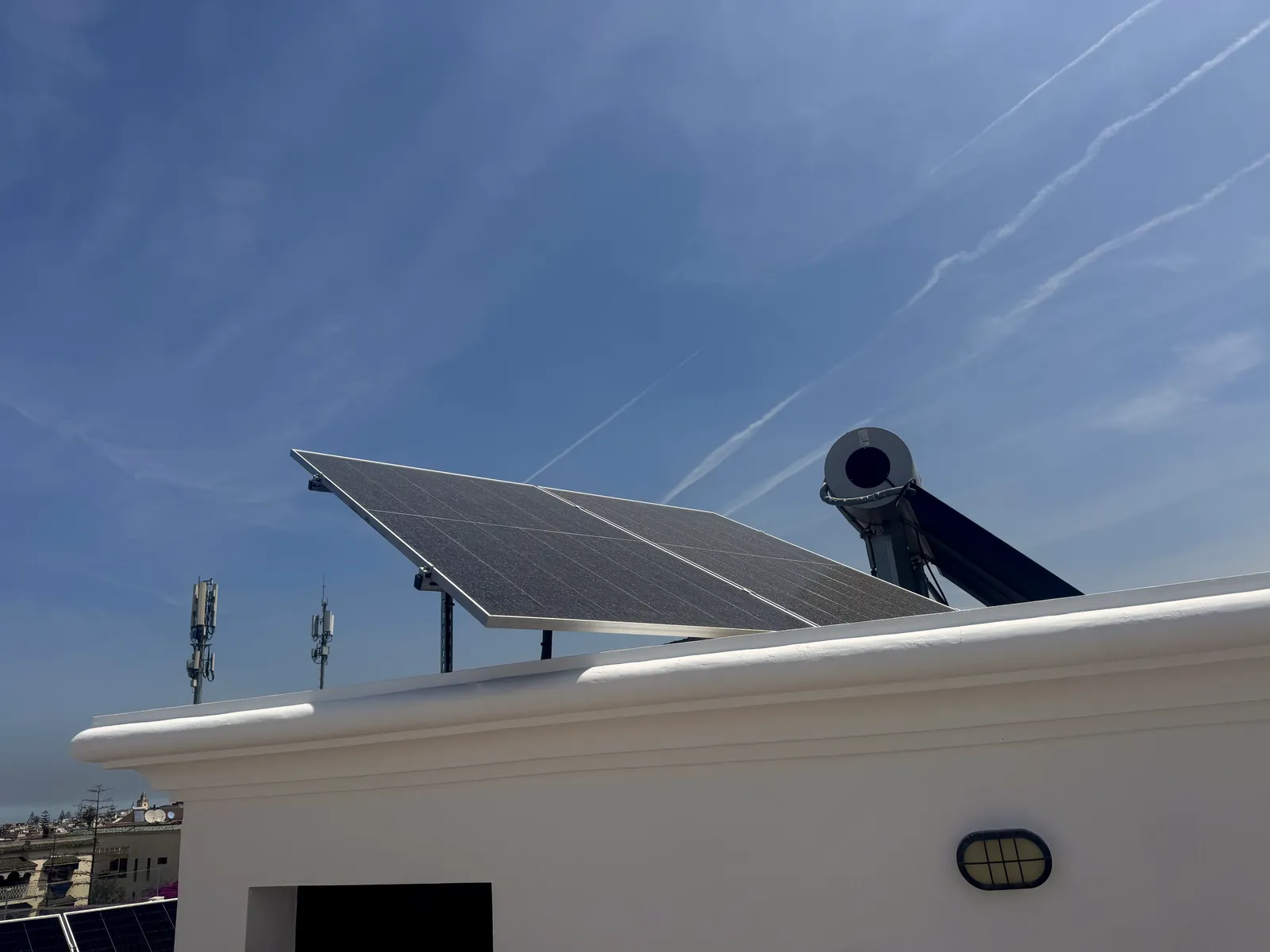 Panneau photovoltaïque et chauffe-eau solaire sur acrotère blanc contre un ciel bleu profond