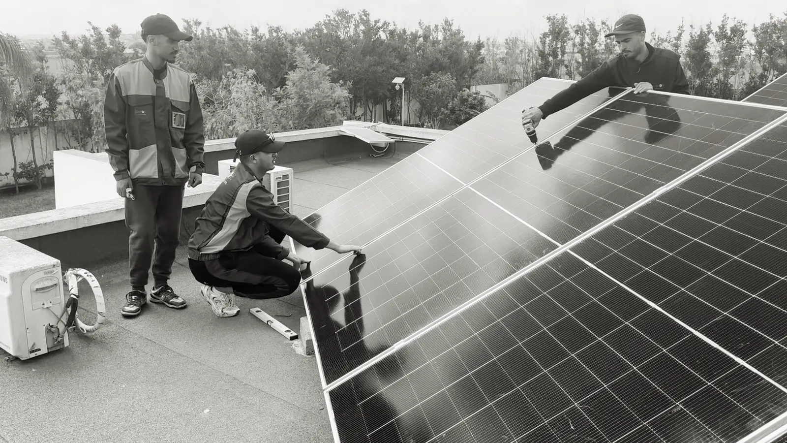 Deux installateurs Taqinor fixant un panneau solaire sur un toit-terrasse